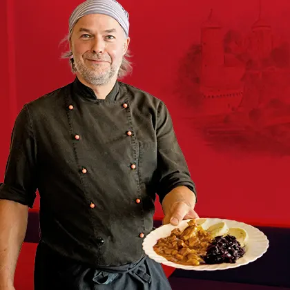 Koch in schwarzer Jacke mit einem Teller Gulasch mit Blaukraut und Böhmischen Knödeln