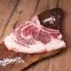 Ein Rib Eye Steak mit Knochen liegt auf einem dunkelbraunen Holzbrett. Daneben liegen grobe Salzkörner.